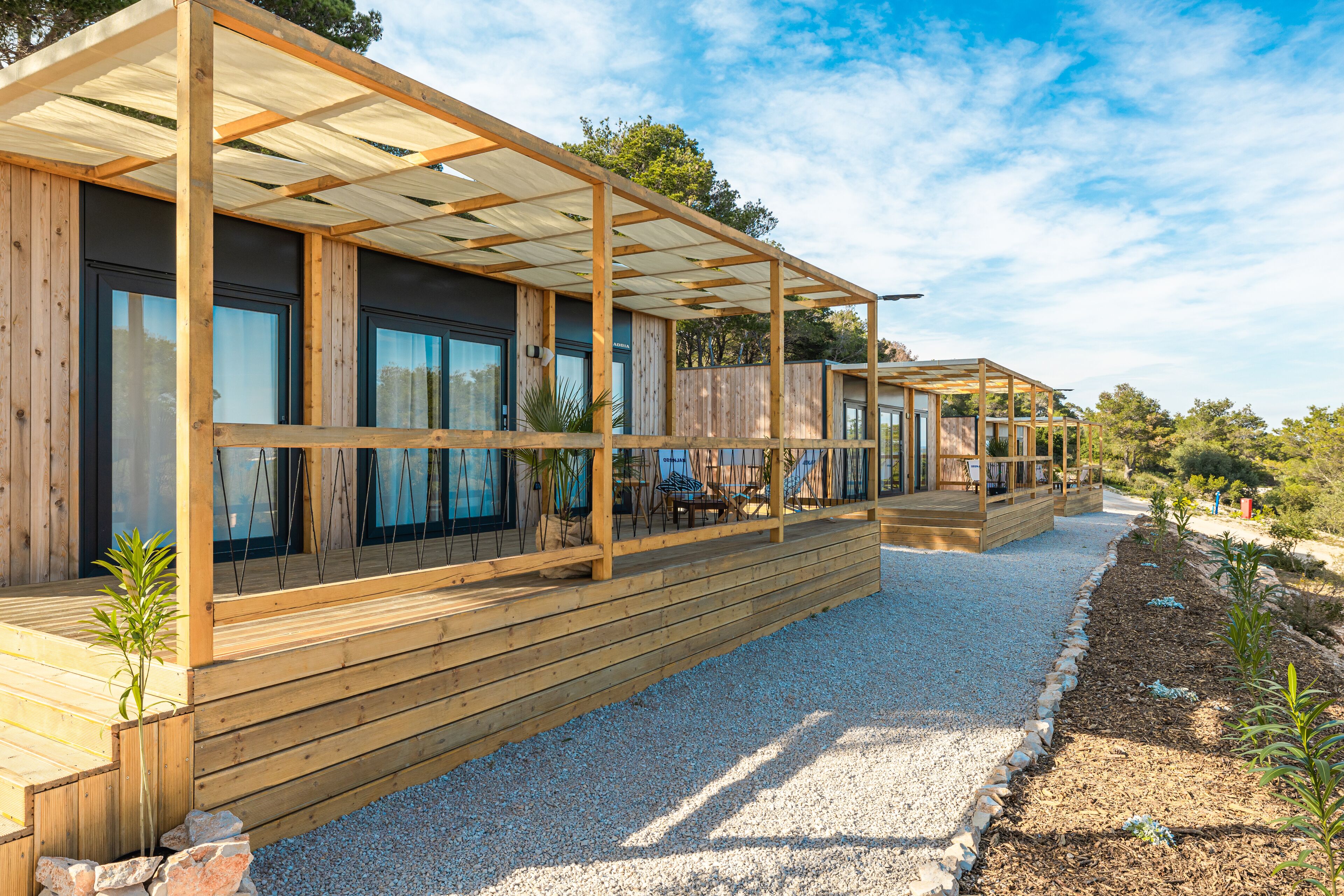 A modern wooden building with a covered outdoor area, gravel pathway, and small plants.