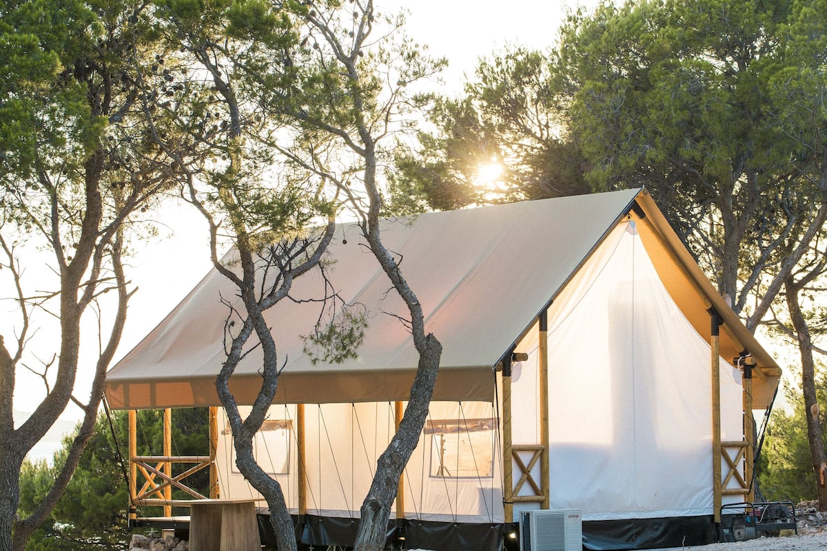A tented accommodation with a simple, functional design, surrounded by trees and set against a natural backdrop.