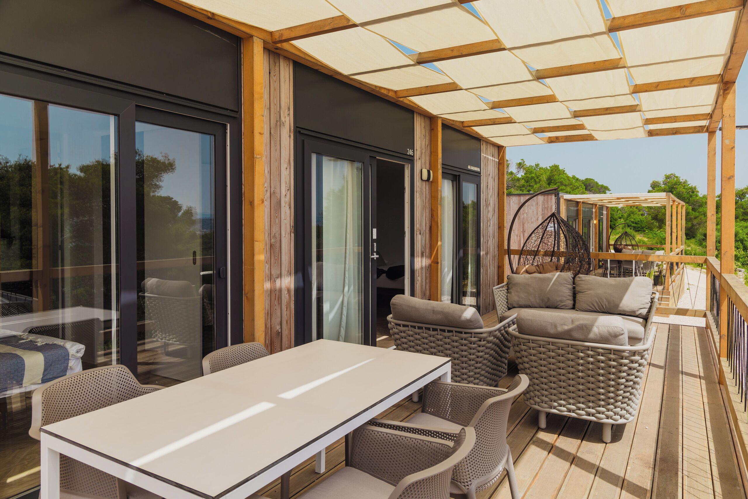 Un patio extérieur couvert, doté d’une table et de meubles en osier, de grandes portes vitrées et d’une terrasse en bois.