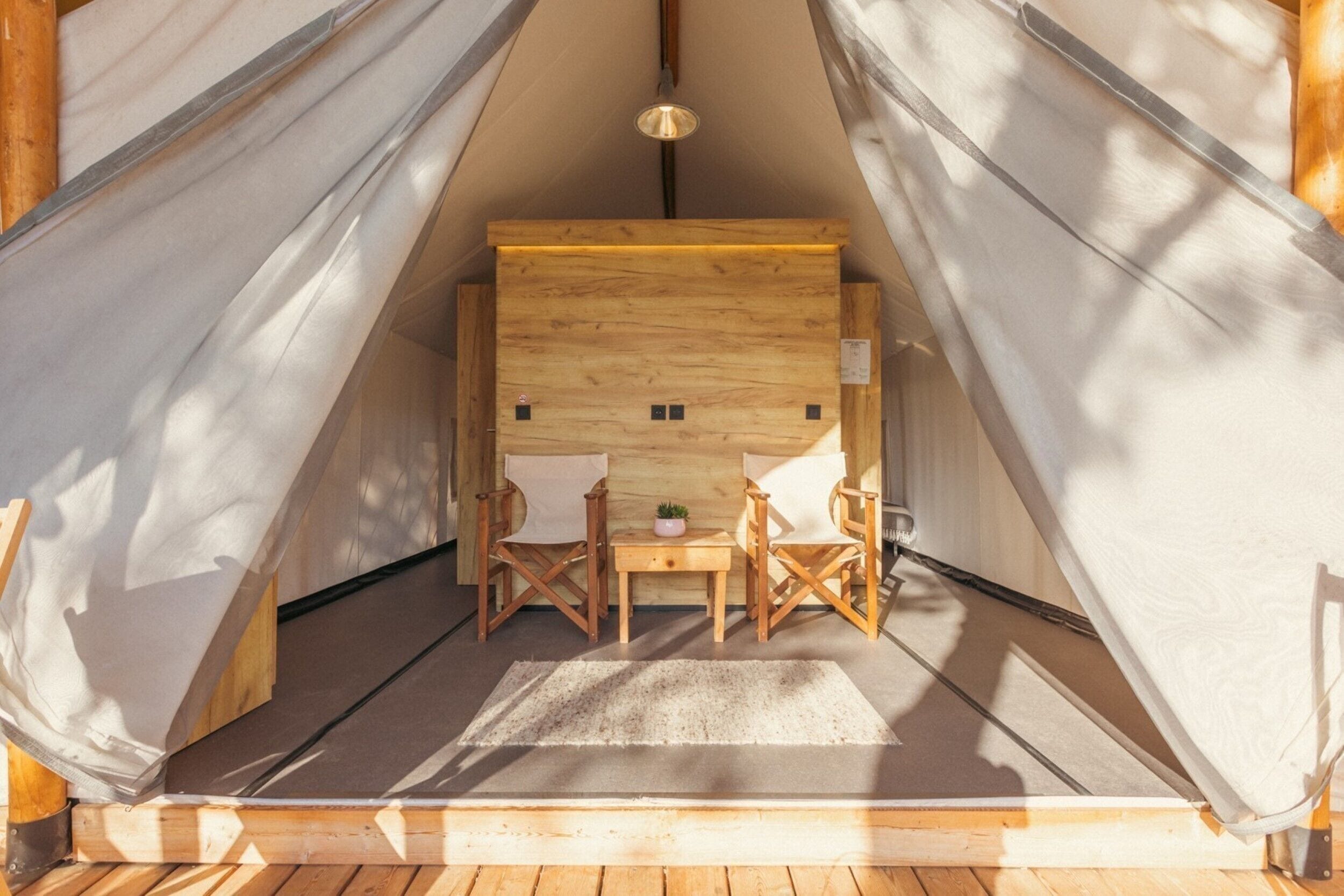 Una carpa con interior de madera, dos sillas, una mesita y una lámpara colgante.