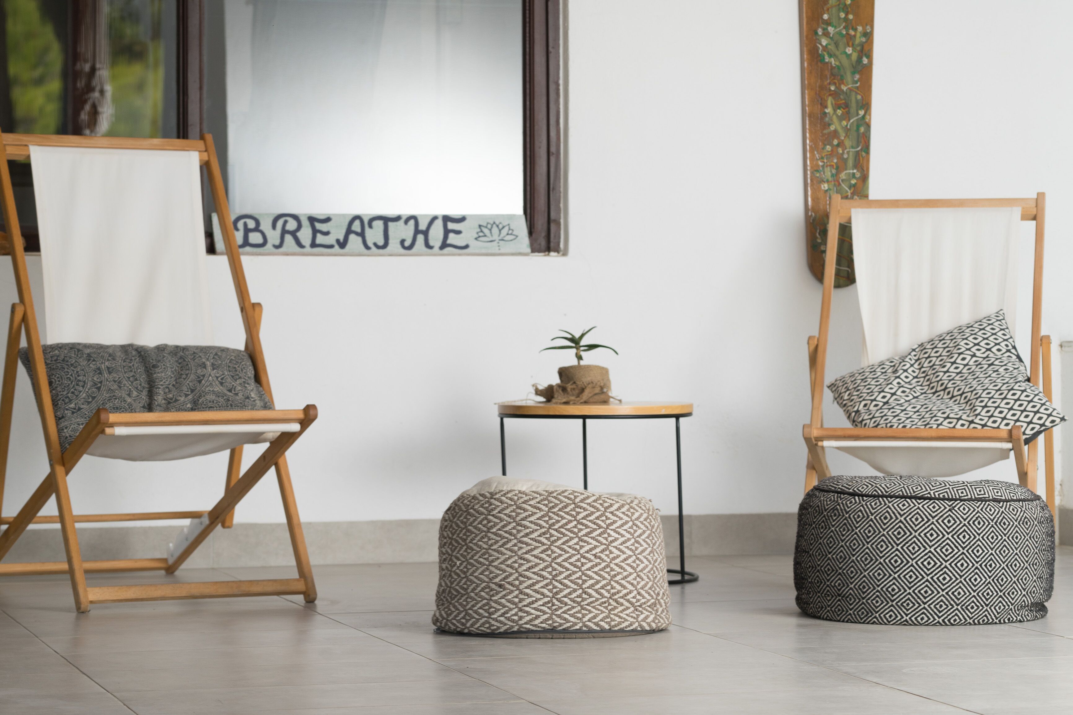 Una habitación con dos sillas de madera, una mesa pequeña con una planta y un cartel que dice 'BREATHE'.