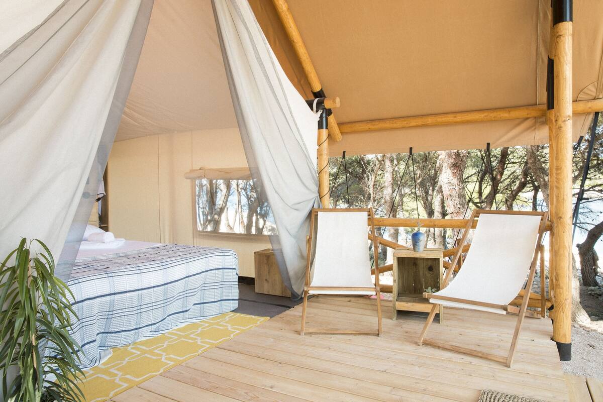 A tented accommodation with a bed, two chairs, and a table.
