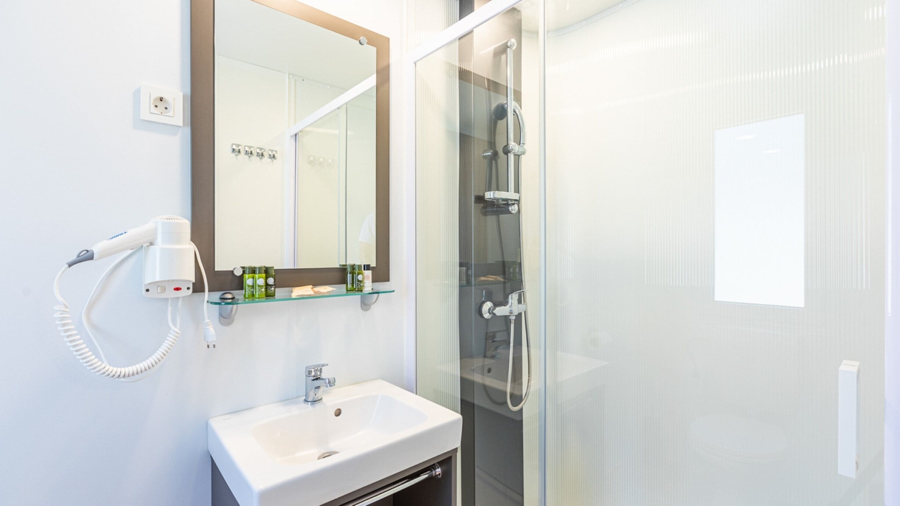 A modern bathroom with a white sink, a hairdryer, and a glass shower enclosure.