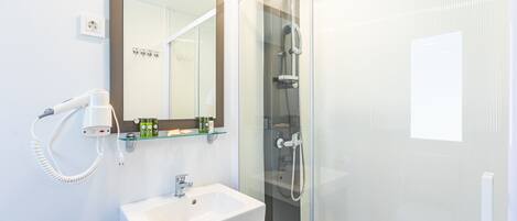 A modern bathroom with a white sink, a hairdryer, and a glass shower enclosure.