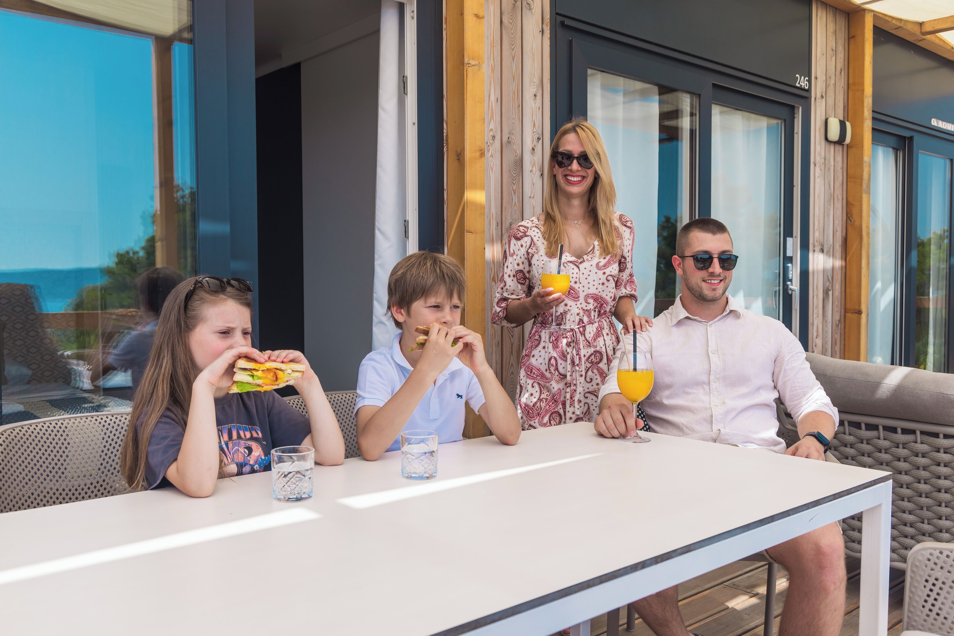 Une famille prend son repas à l’extérieur, à une table d’où l’on peut admirer la mer.