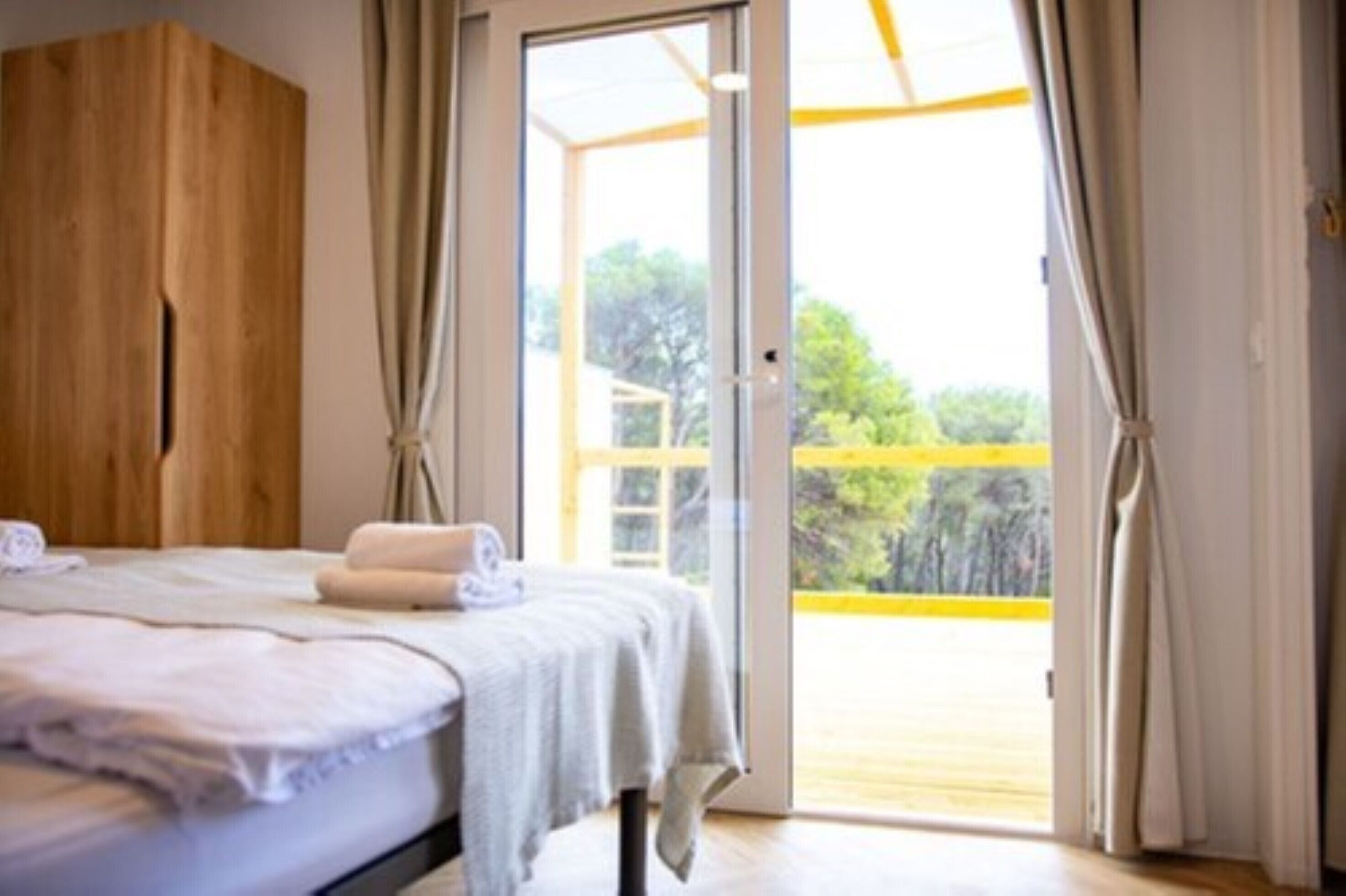 Quarto com cama, guarda-roupa de madeira e porta de correr de vidro que dá para uma área externa.