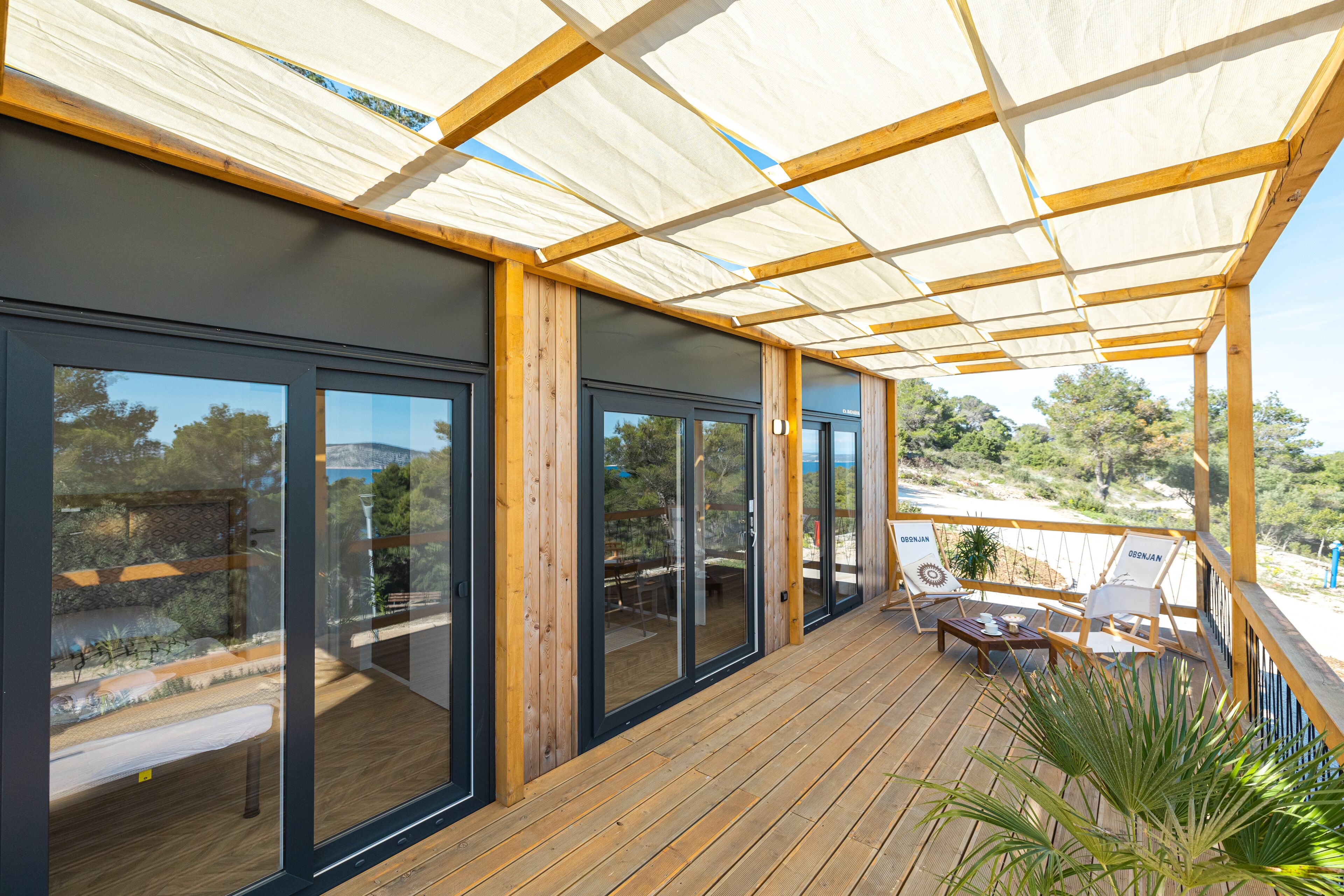 A covered outdoor area with wooden flooring, large sliding glass doors, and a seating area with two chairs and a table.