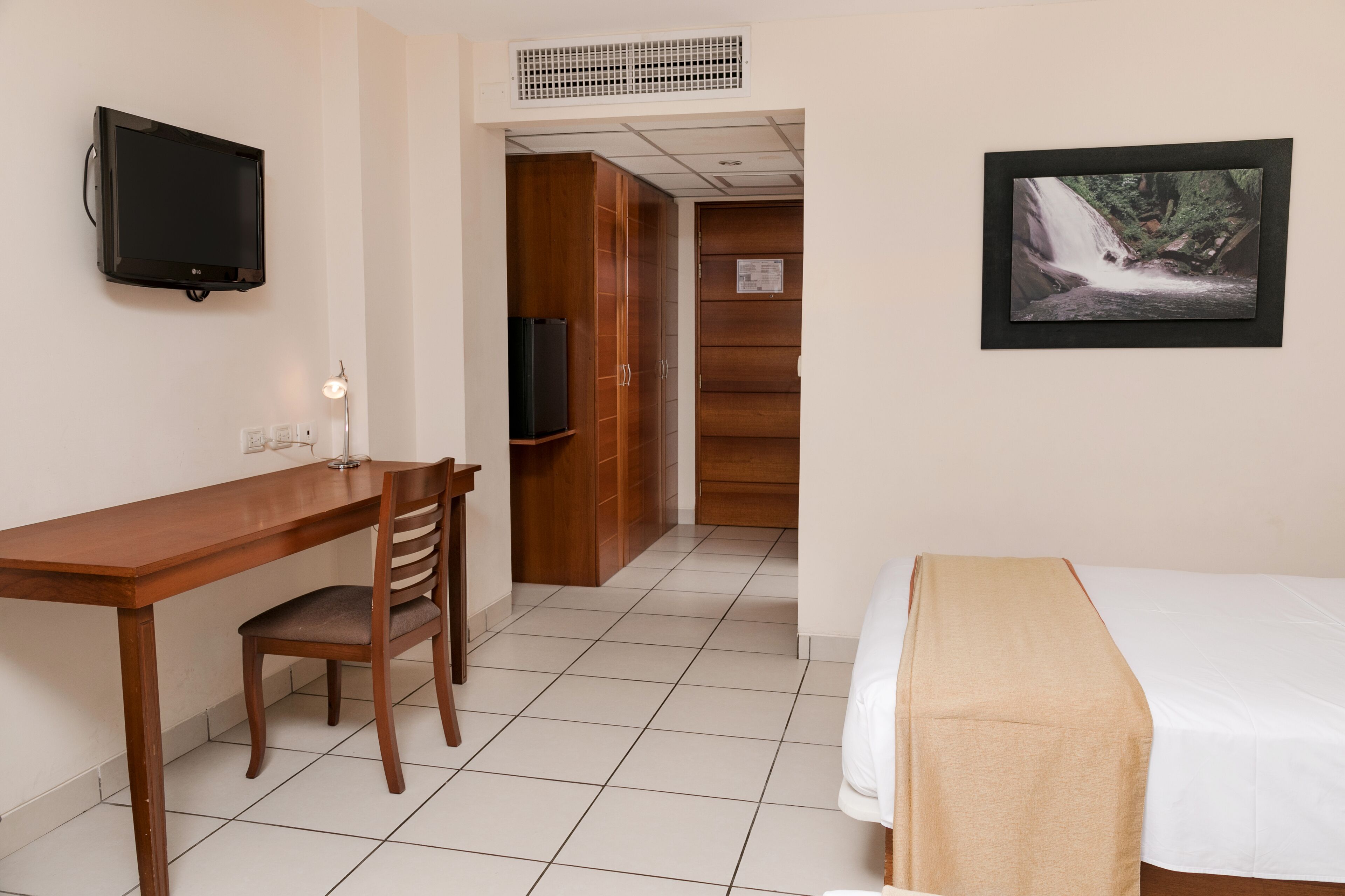 Une chambre d’hôtel avec un lit, un bureau et une chaise, une télévision et un tableau encadré au mur.