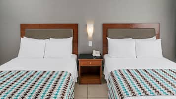 Une chambre d’hôtel avec deux lits, chacun recouvert d’une literie blanche et d’une couverture à motifs. Une table de chevet se trouve entre les deux lits, avec un téléphone et un petit tiroir.