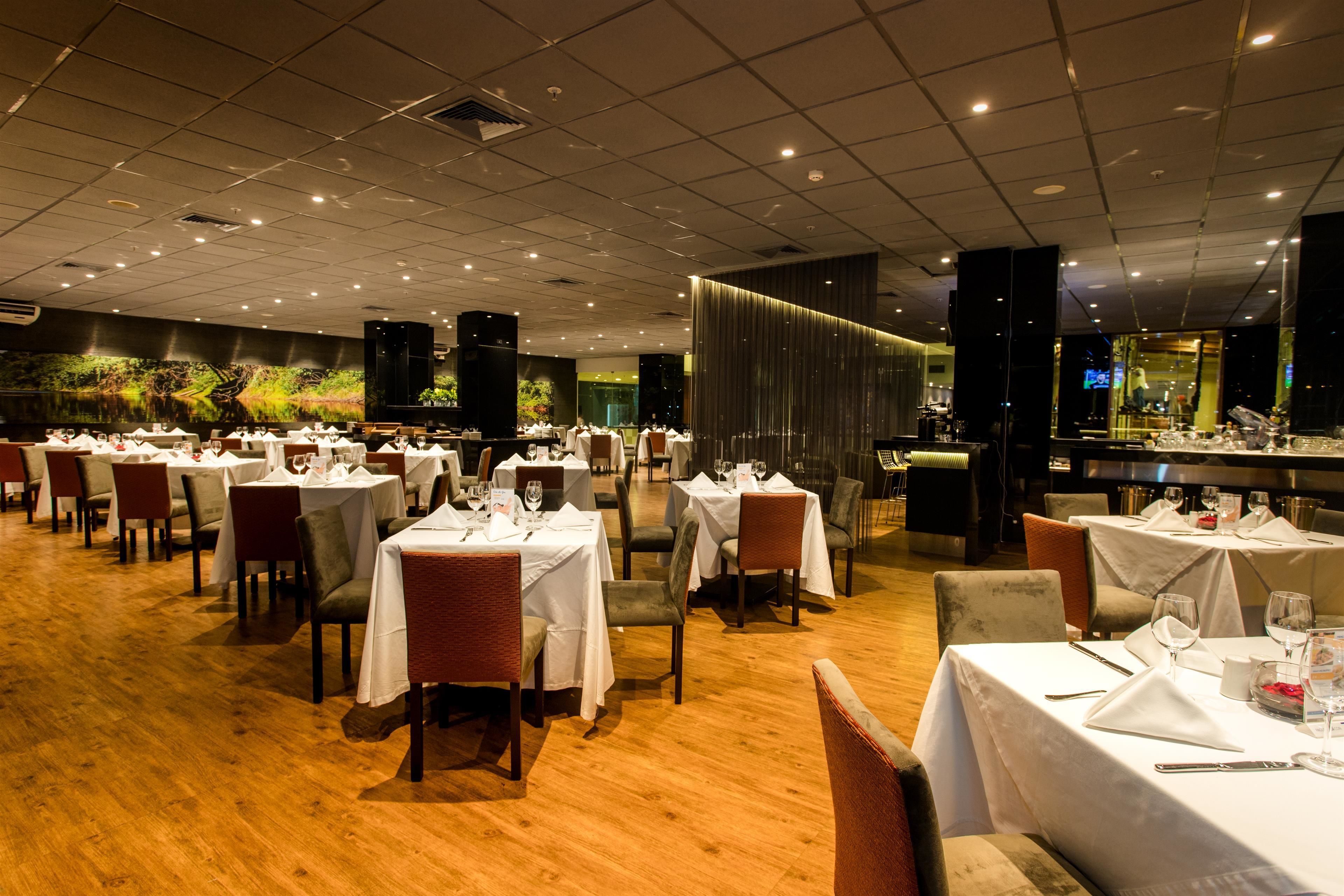 A restaurant with multiple tables set for dining, featuring a modern interior with wooden flooring and a bar area.