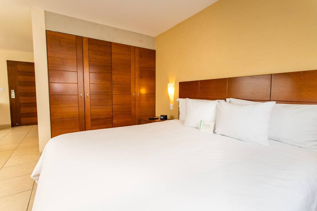 Una habitación de hotel con una cama grande, un armario de madera y una mesita de noche con control remoto.