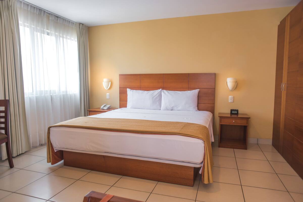 Een hotelkamer met een groot bed, twee nachtkastjes, een houten garderobe en een raam met gordijnen.