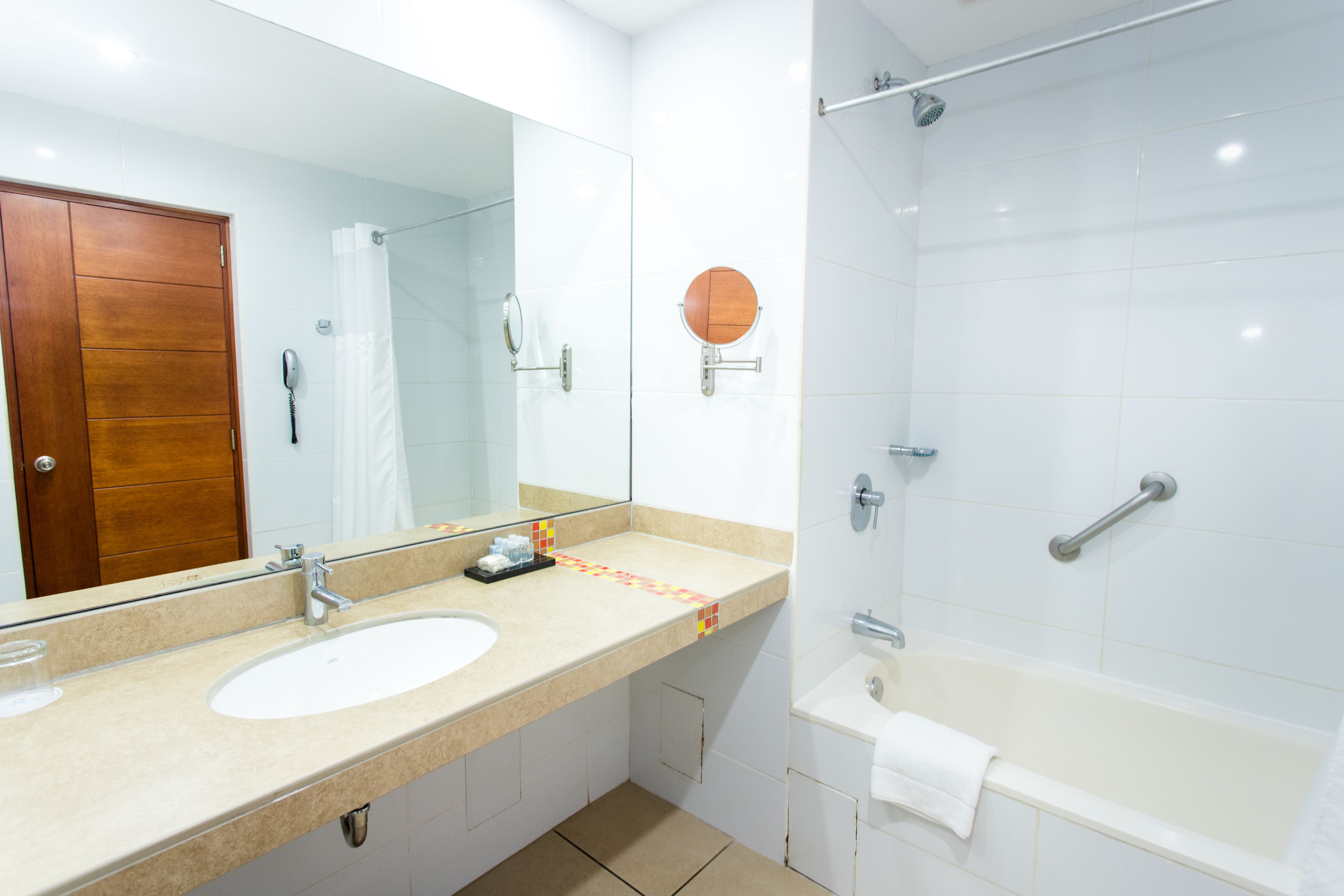 A modern bathroom with a large mirror, two sinks, a shower, and a bathtub.