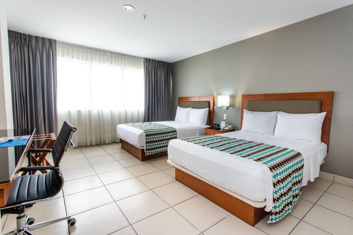 Een hotelkamer met twee bedden, een bureau, een stoel en een raam met gordijnen.