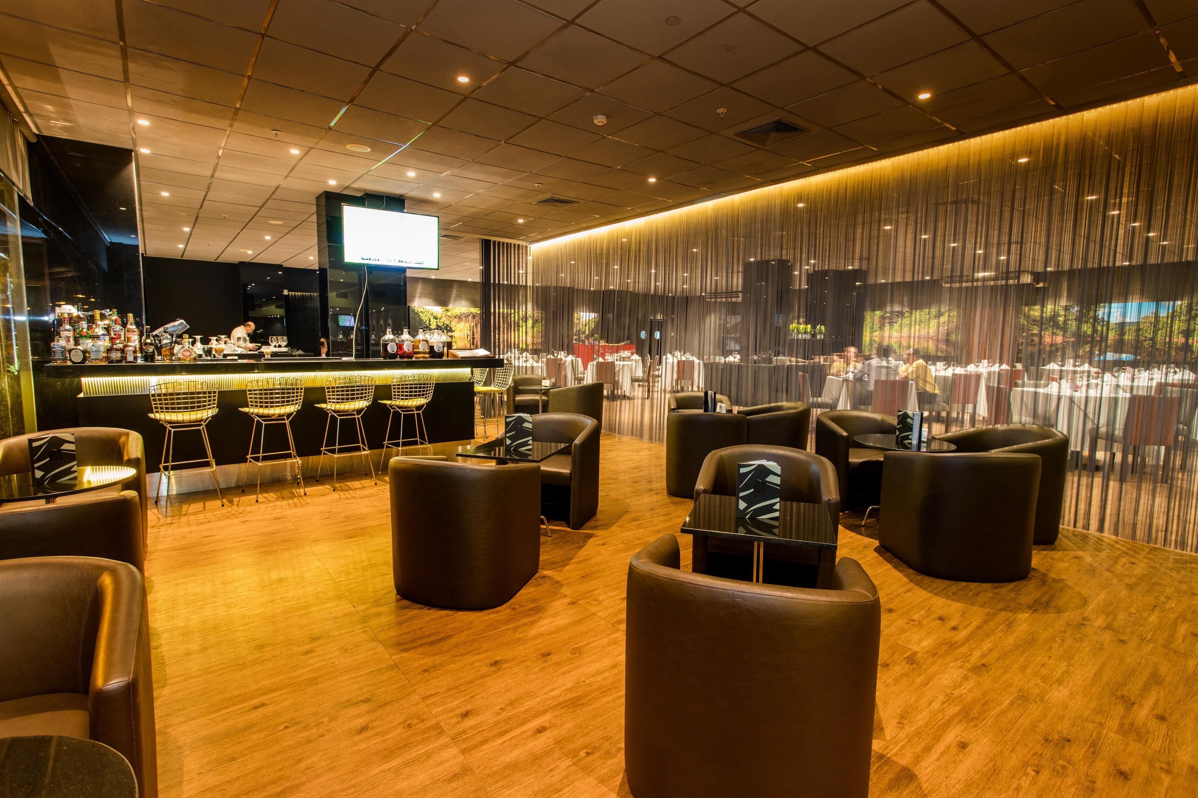 A modern bar area with a wooden floor, leather seating, and a large screen displaying content.