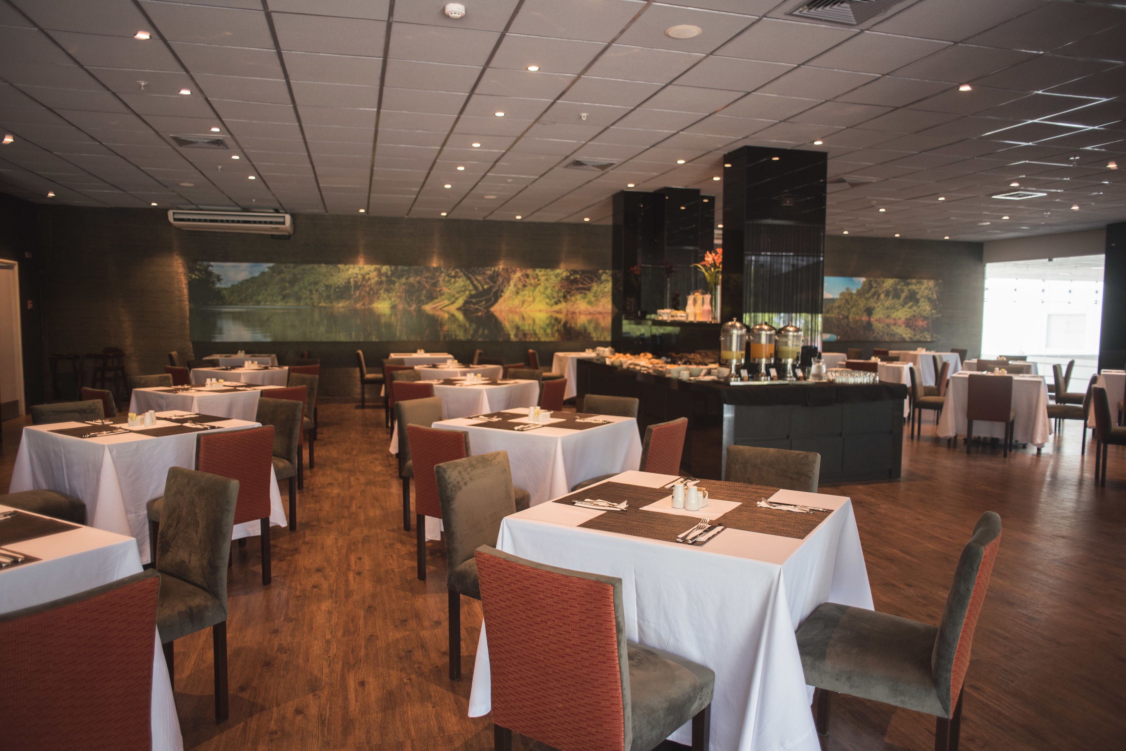 A restaurant with multiple tables and chairs, a bar area, and a large screen displaying a nature scene.