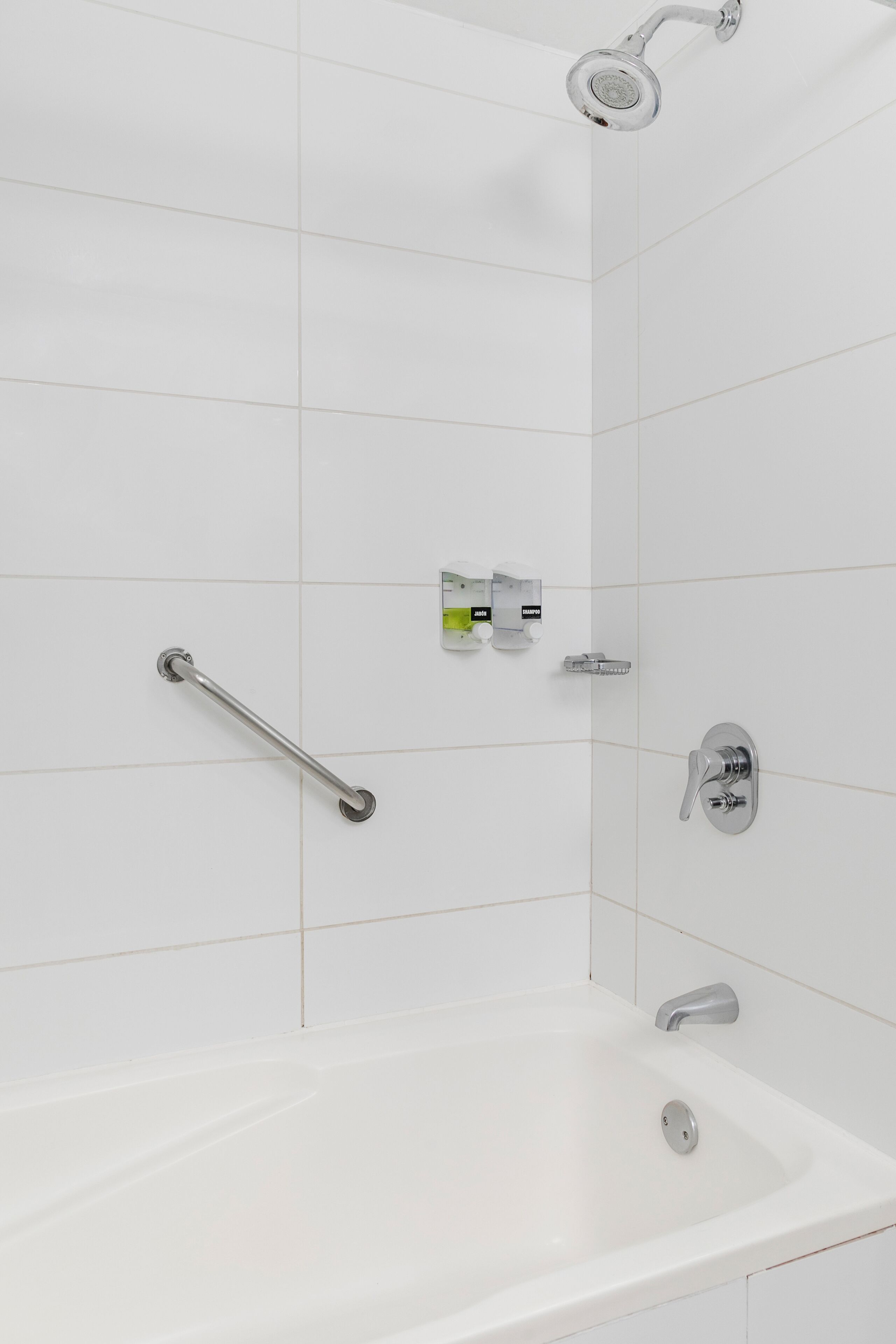 A modern bathroom with a white bathtub, a handheld showerhead, a handheld shower attachment, and a grab bar.