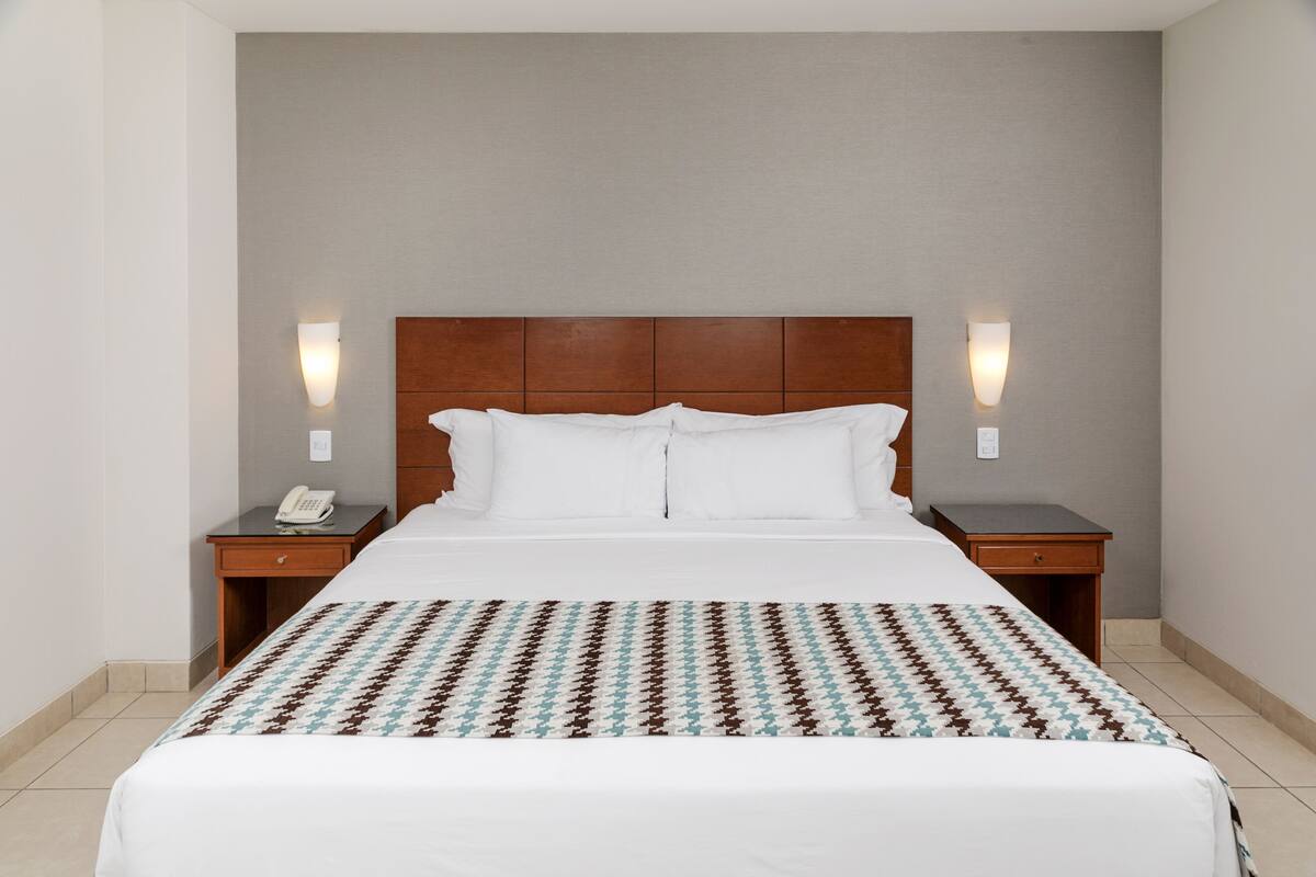 Een hotelkamer met een groot bed, twee nachtkastjes, een telefoon en wandlampen.