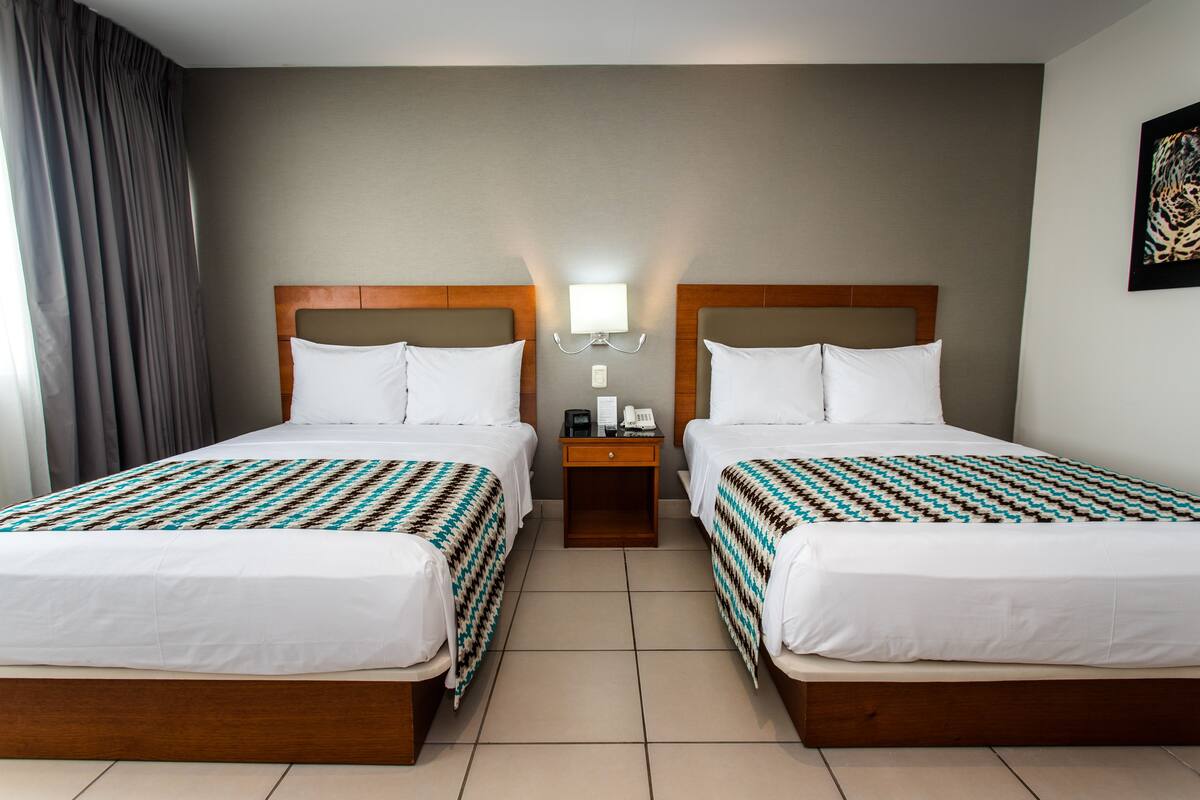 Een hotelkamer met twee bedden, een nachtkastje, een lamp en een schilderij aan de muur.
