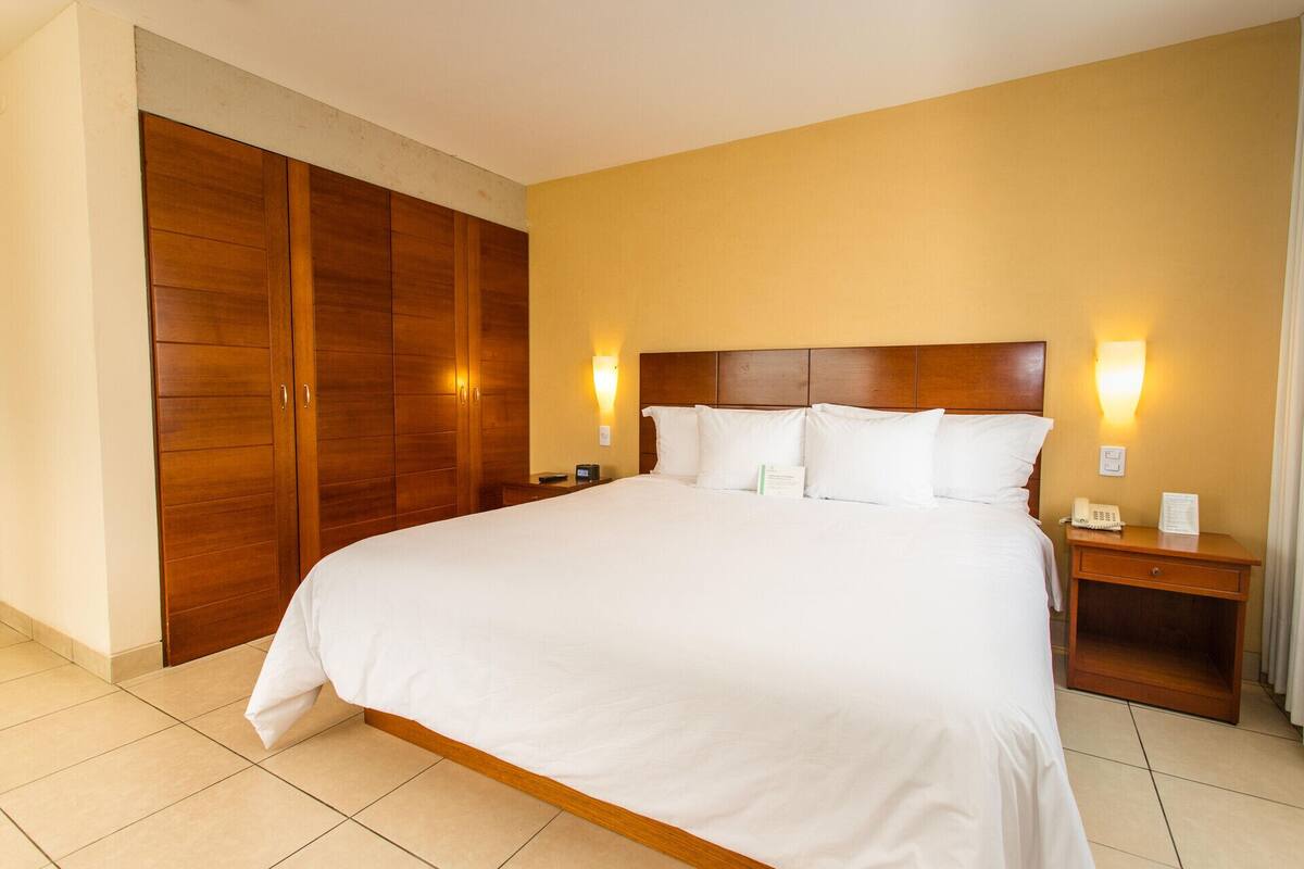 Een hotelkamer met een groot bed, een houten garderobe, nachtkastjes en wandlampen.