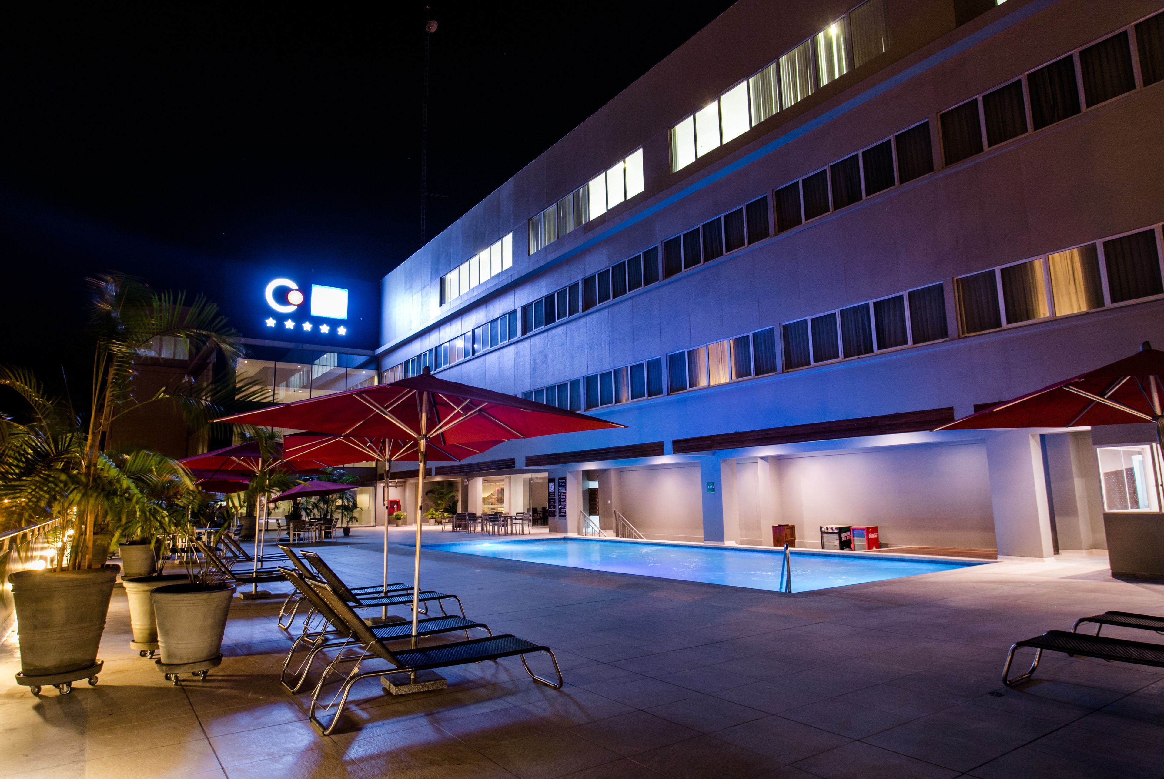 Ein Hotel mit Schwimmbad, Sitzgelegenheiten im Freien und Sonnenschirmen.