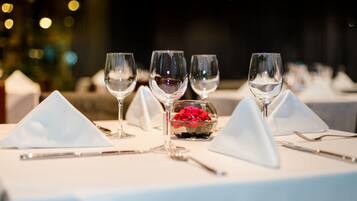 Una mesa lista para comer con copas de vino, un cuenco pequeño con flores rojas y servilletas blancas.
