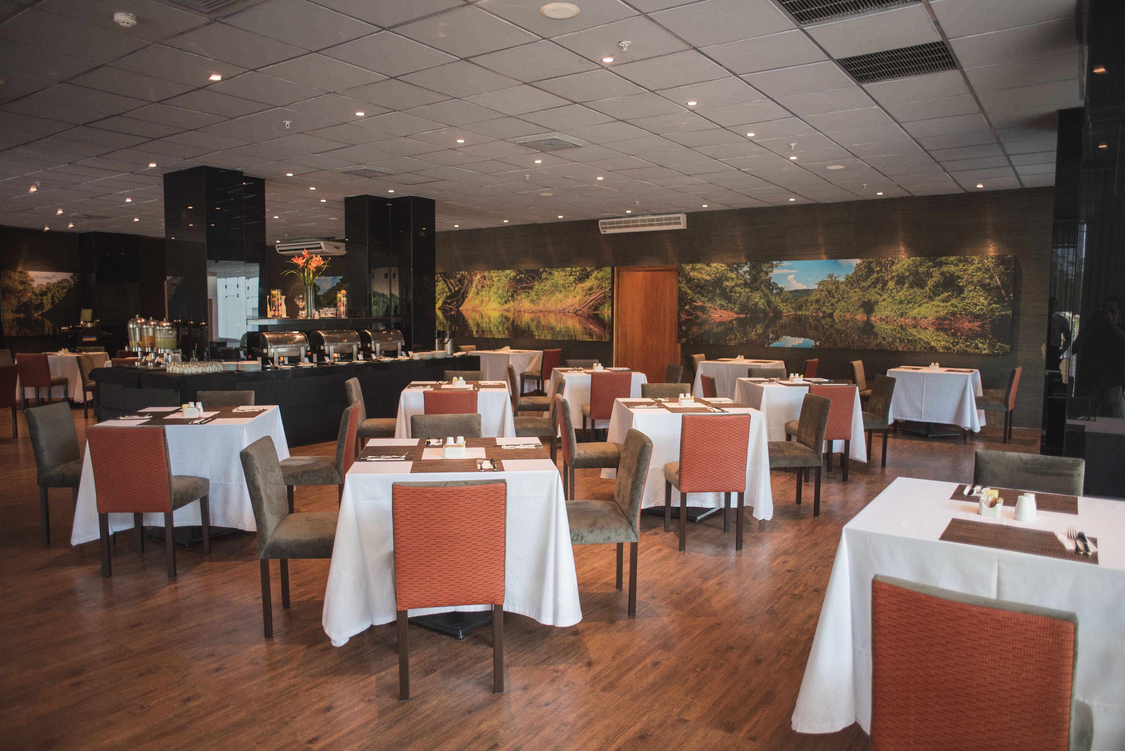 A restaurant with multiple tables and chairs, a bar area, and a large mural on the wall.
