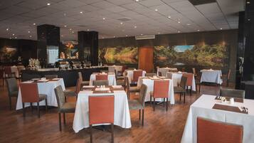 A restaurant with multiple tables and chairs, a bar area, and a large mural on the wall.