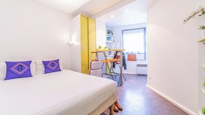 A bedroom with a bed, two purple pillows, a yellow door, a small table with chairs, and a window. - Montempô Apparthôtel Evry (Évry-Courcouronnes)