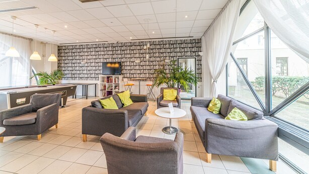 A modern living room with grey sofas, a coffee table, and a bookshelf filled with books. - Montempô Apparthôtel Evry (Évry-Courcouronnes)