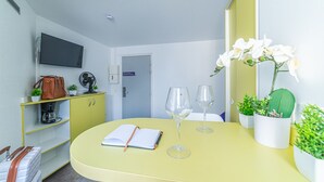 A compact room with a yellow table, a TV mounted on the wall, a coffee machine, a small cabinet, and a door with a sign. - Montempô Apparthôtel Evry (Évry-Courcouronnes)