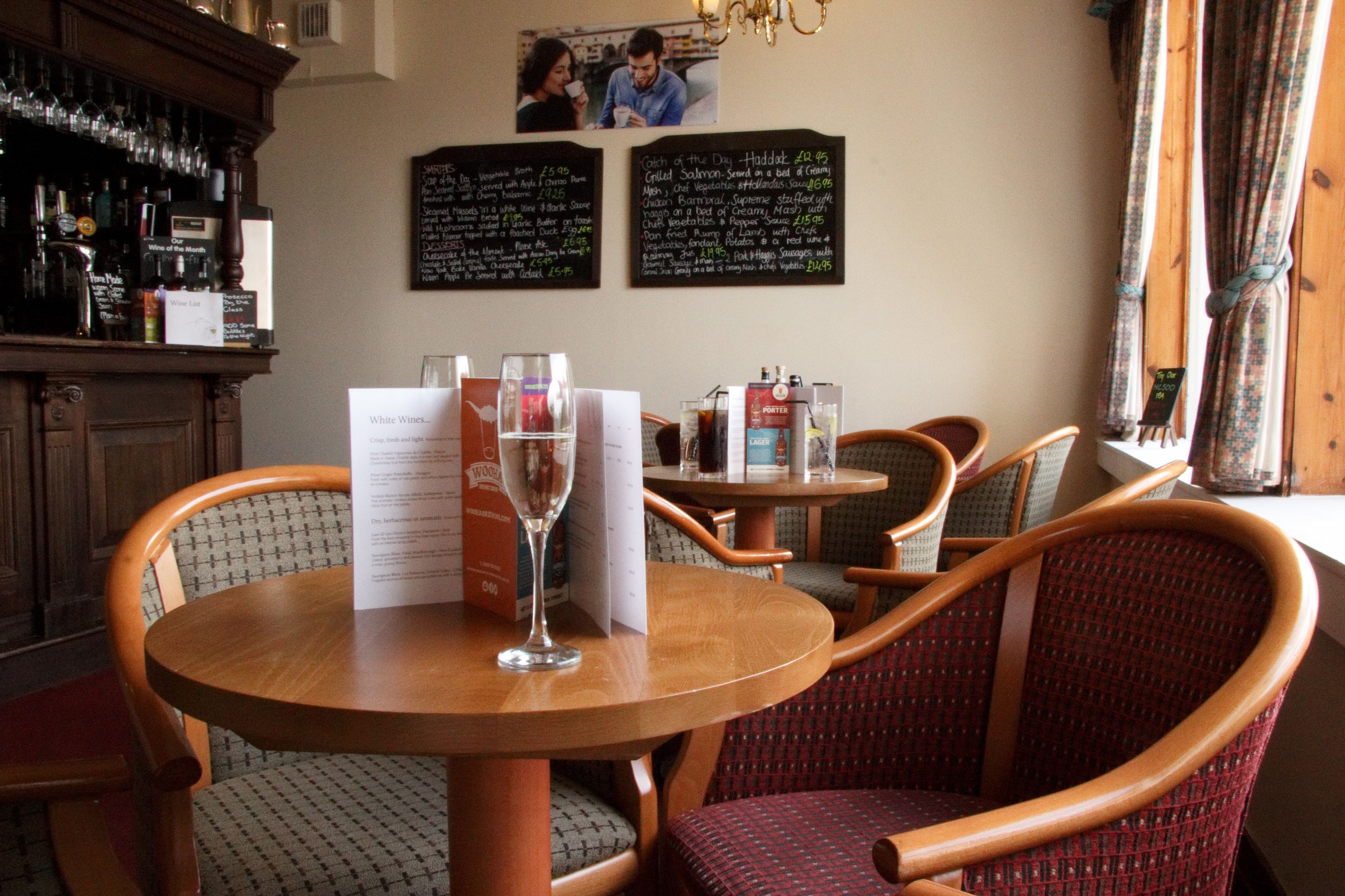 A restaurant interior with round wooden tables, wicker chairs, and a menu on the table.