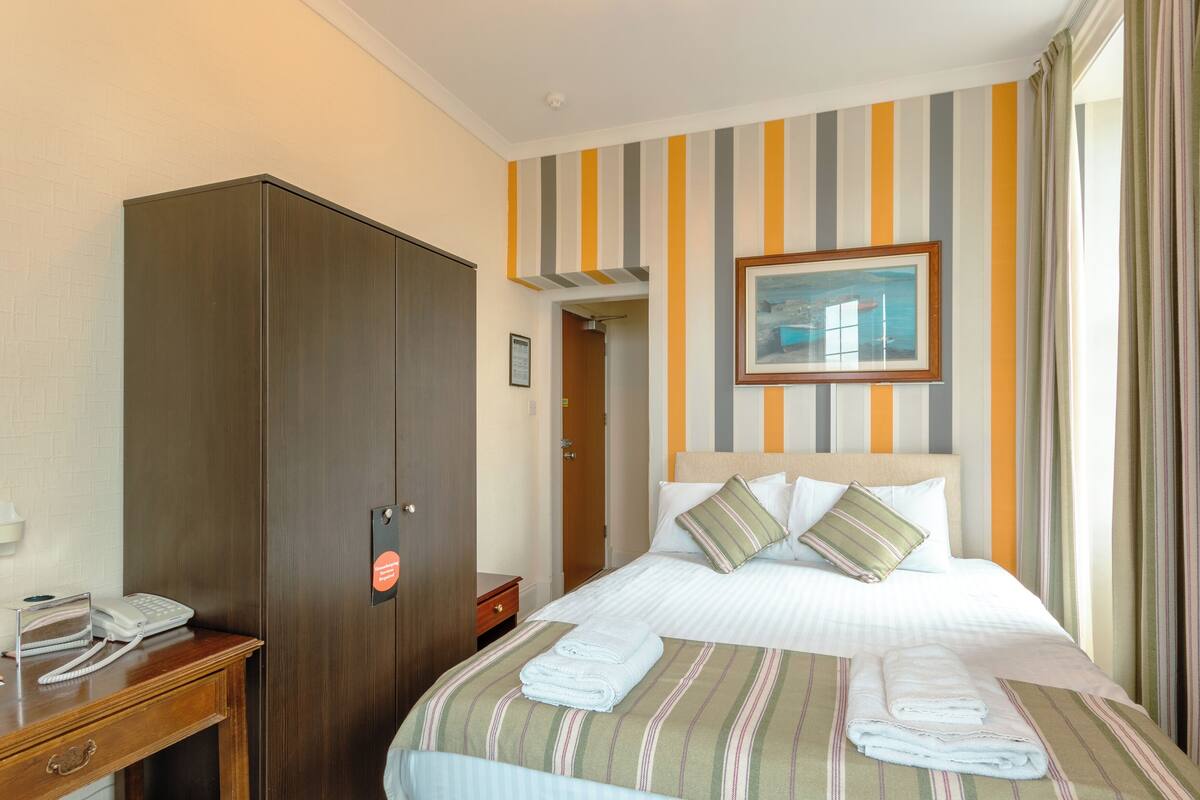 Een hotelkamer met een bed, een kledingkast, een nachtkastje met telefoon en een lijst aan de muur.