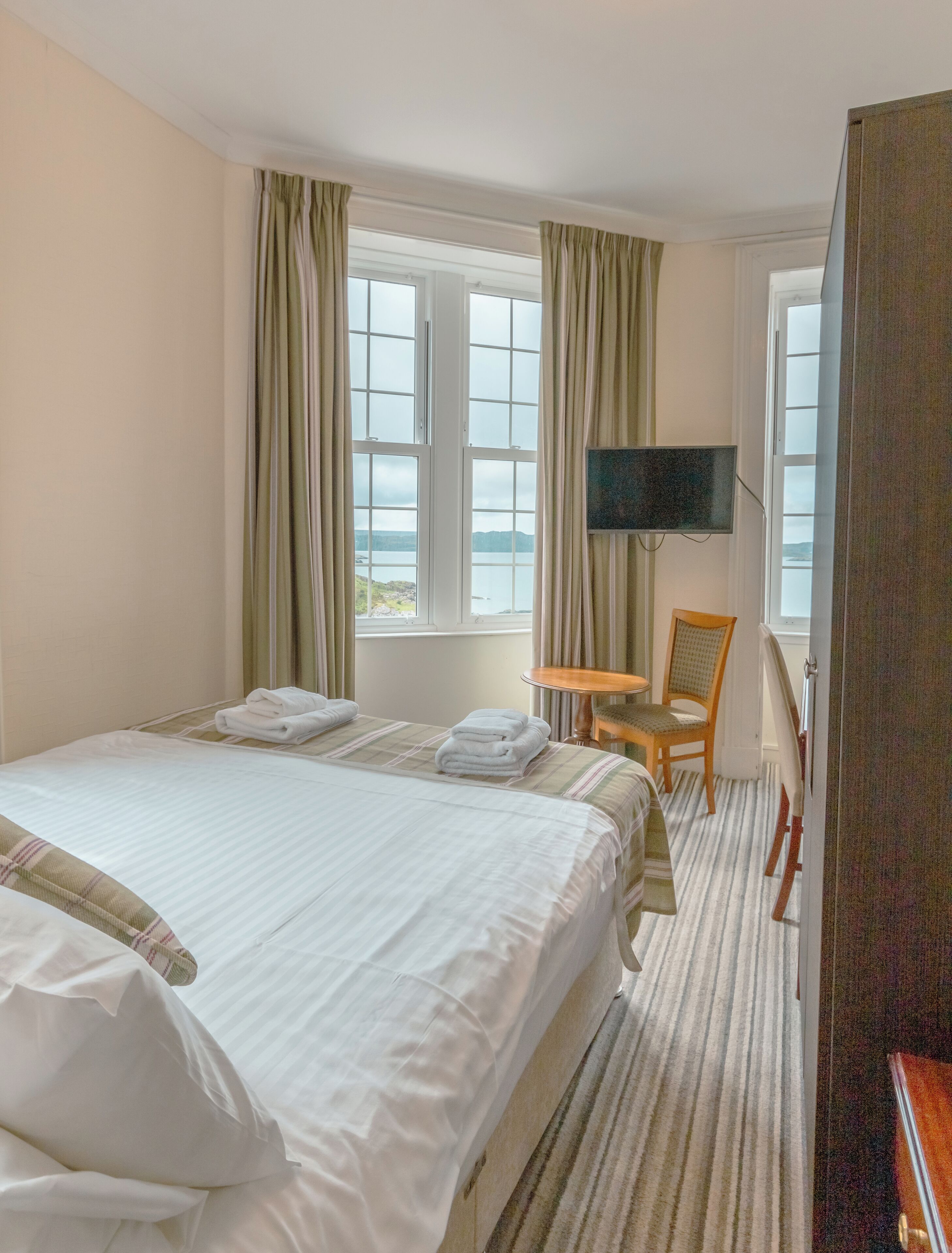 Ein Hotelzimmer mit Bett, Sessel, Fernseher und einem Fenster mit Vorhängen.