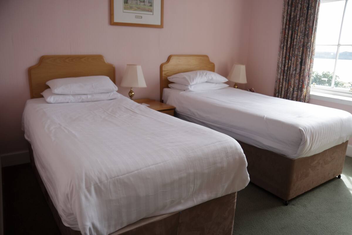 Een hotelkamer met twee eenpersoonsbedden, houten hoofdeinden, bedlampen en een raam met gordijnen.