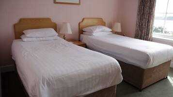 Quarto de hotel com duas camas de solteiro, cabeceiras de madeira, abajures e uma janela com cortinas.