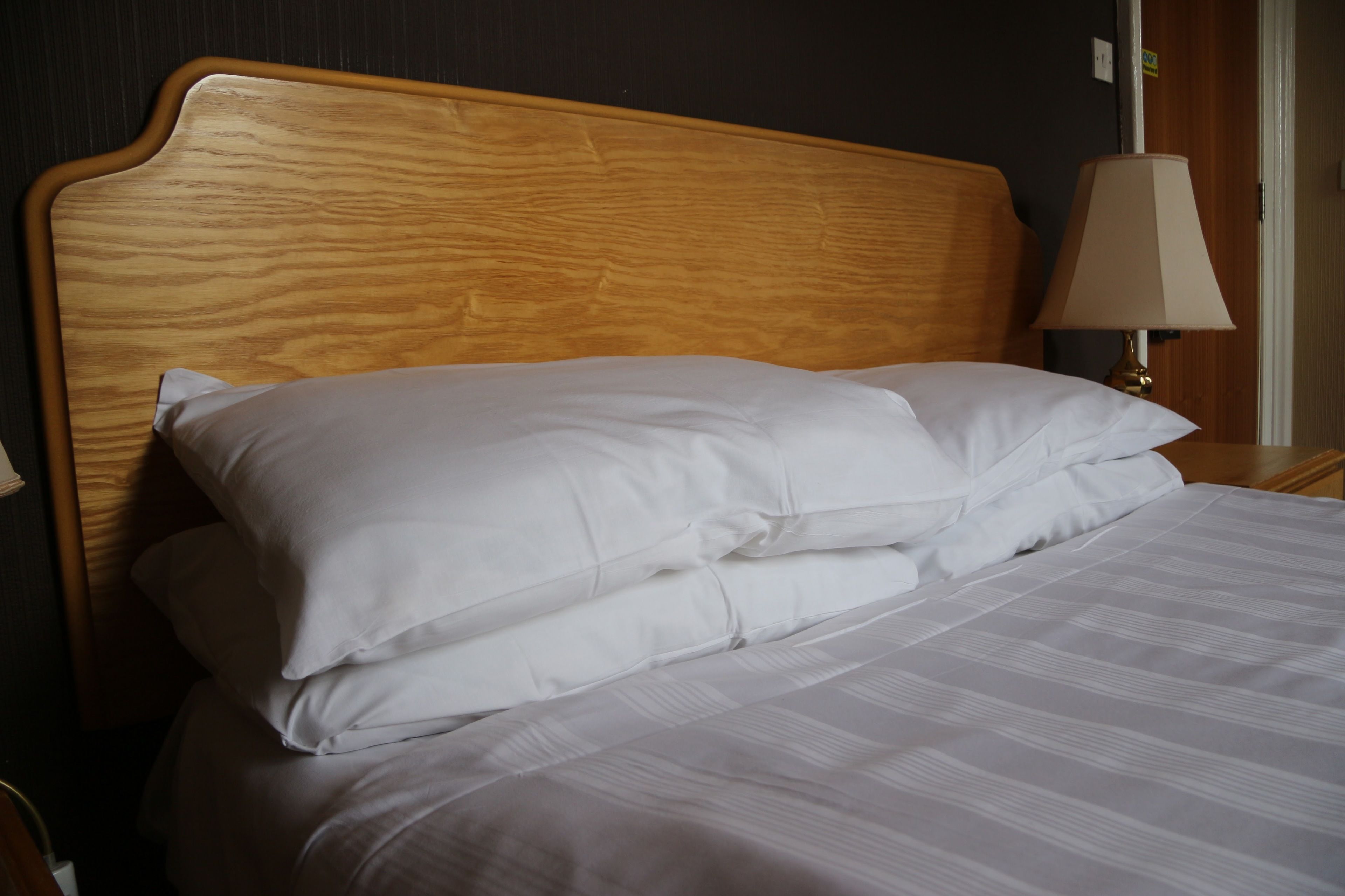 Cama bem arrumada com lençóis brancos e cabeceira de madeira.