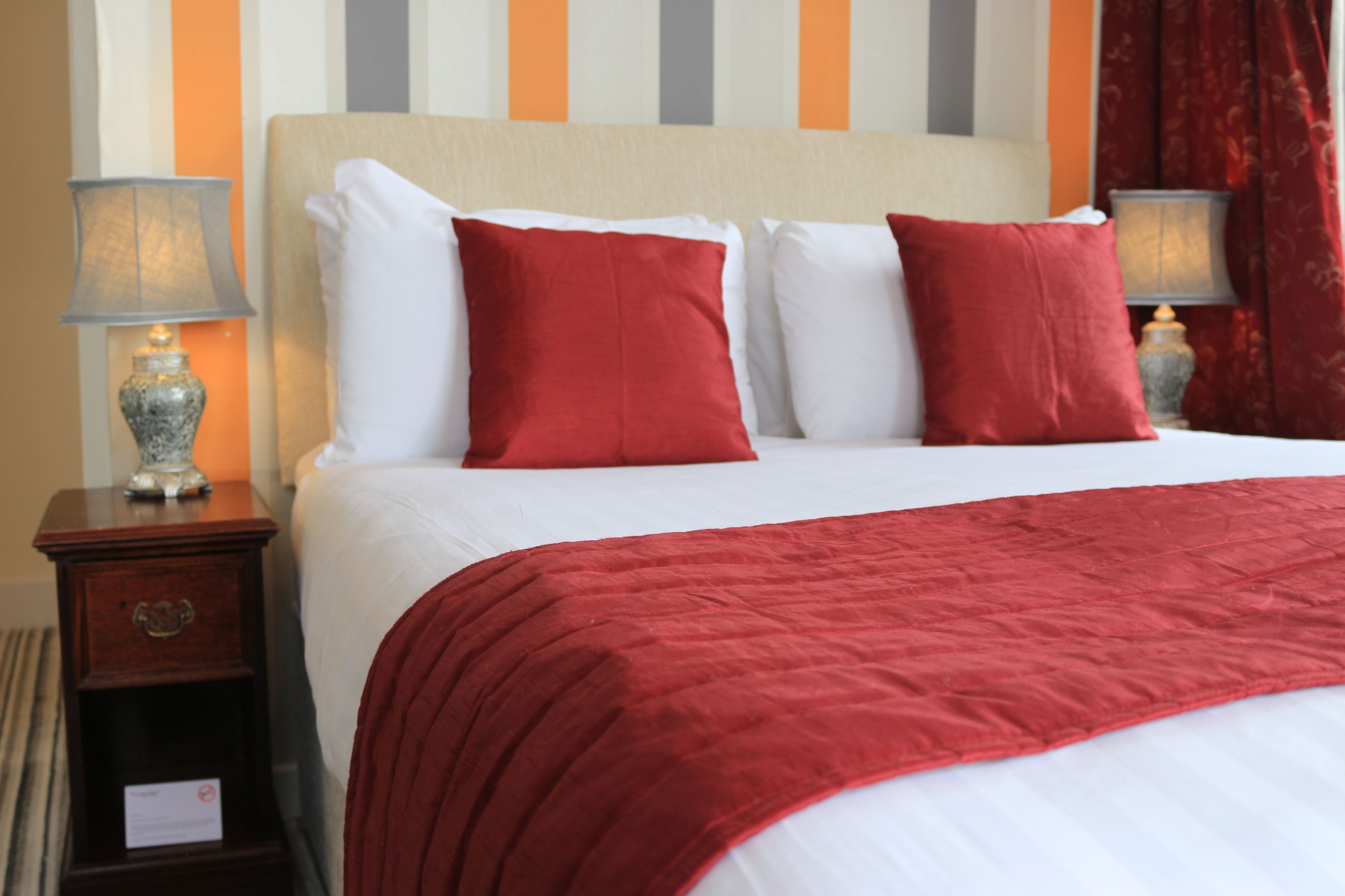 A hotel room with a large bed, red and white bedding, and two bedside lamps.