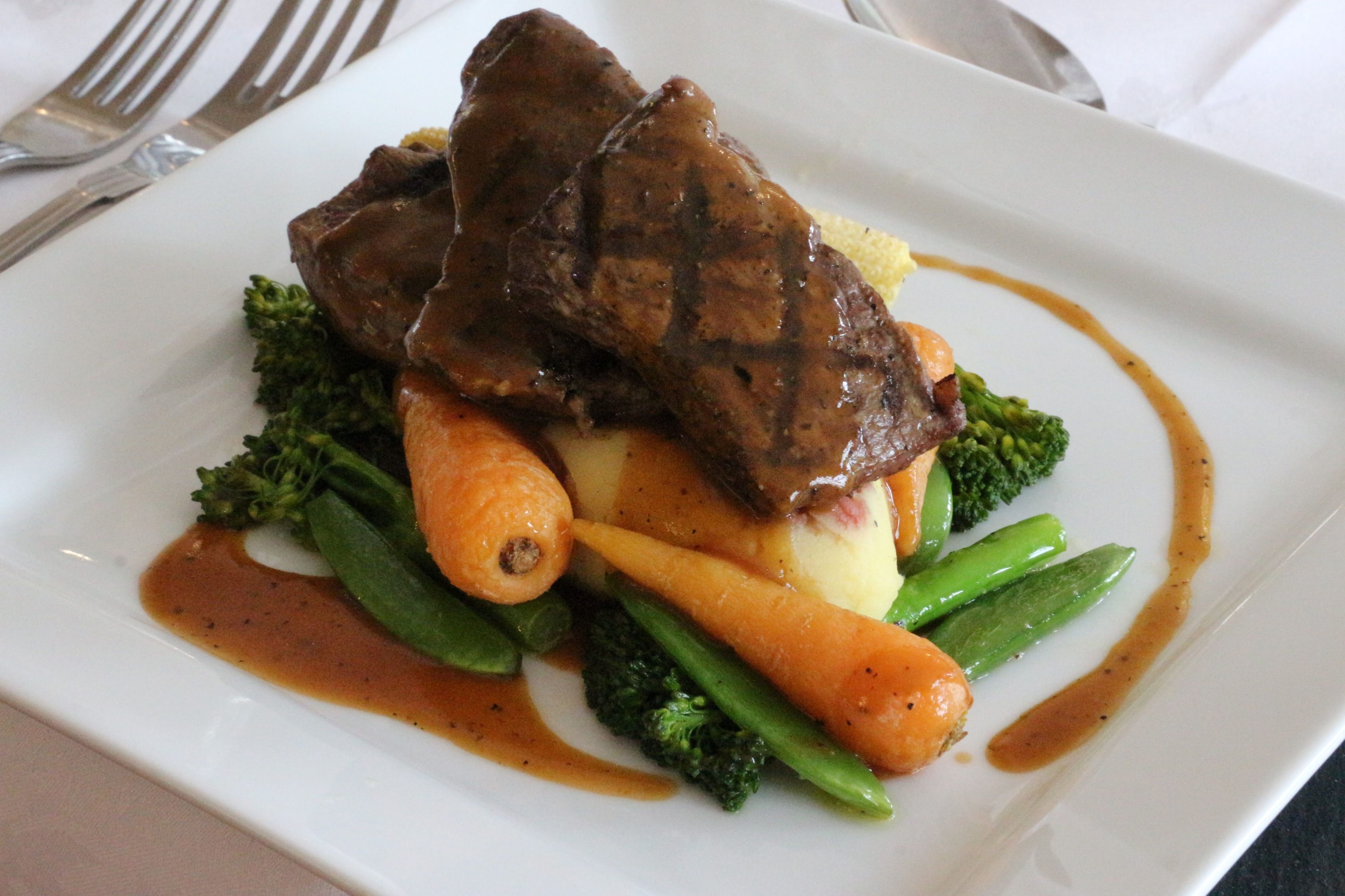 A white plate with a beef steak, carrots, broccoli, and potatoes, garnished with sauce.