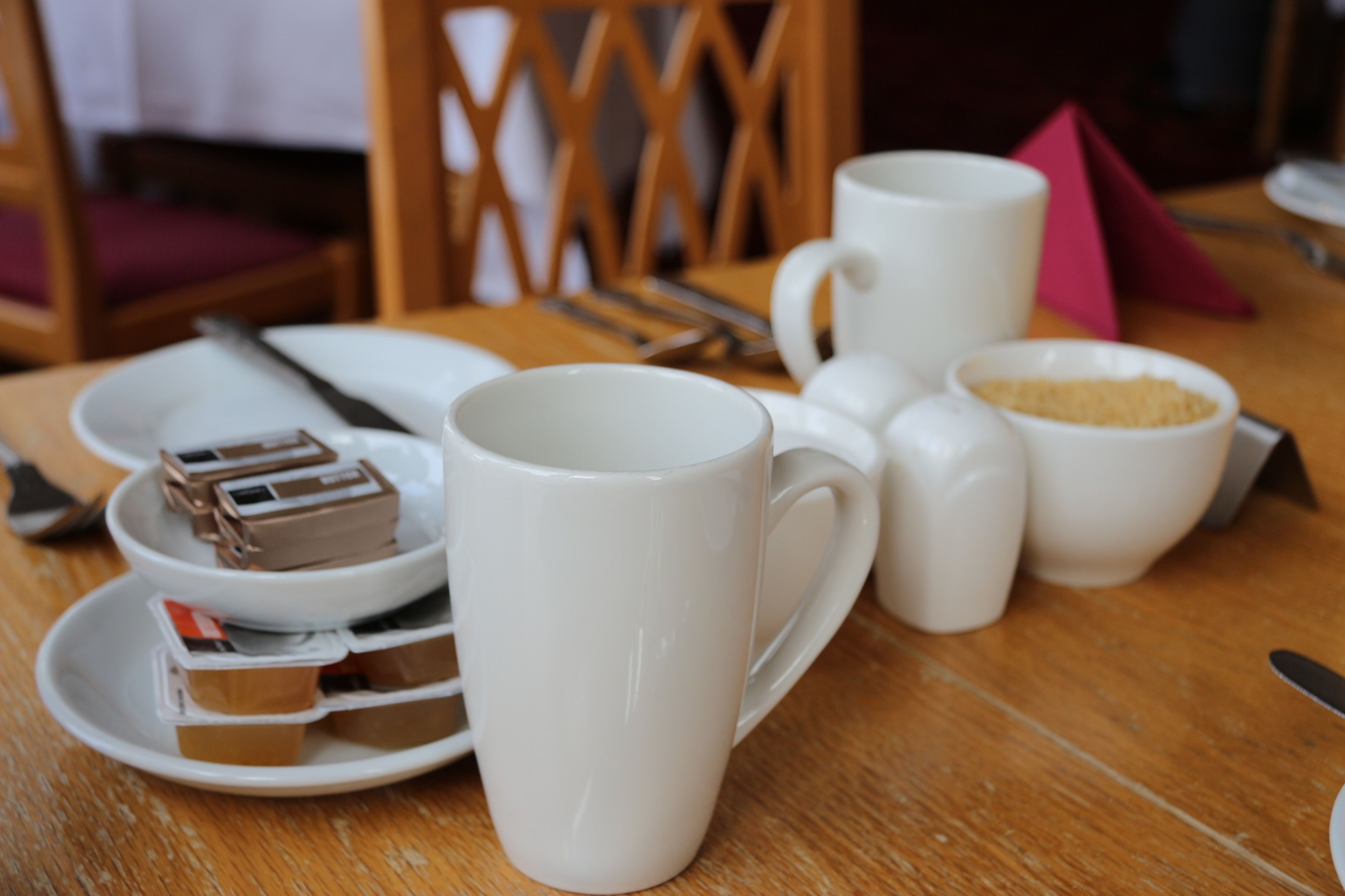 Una mesa con una taza blanca, un plato con un postre de chocolate y un cuenco de cubitos de azúcar.