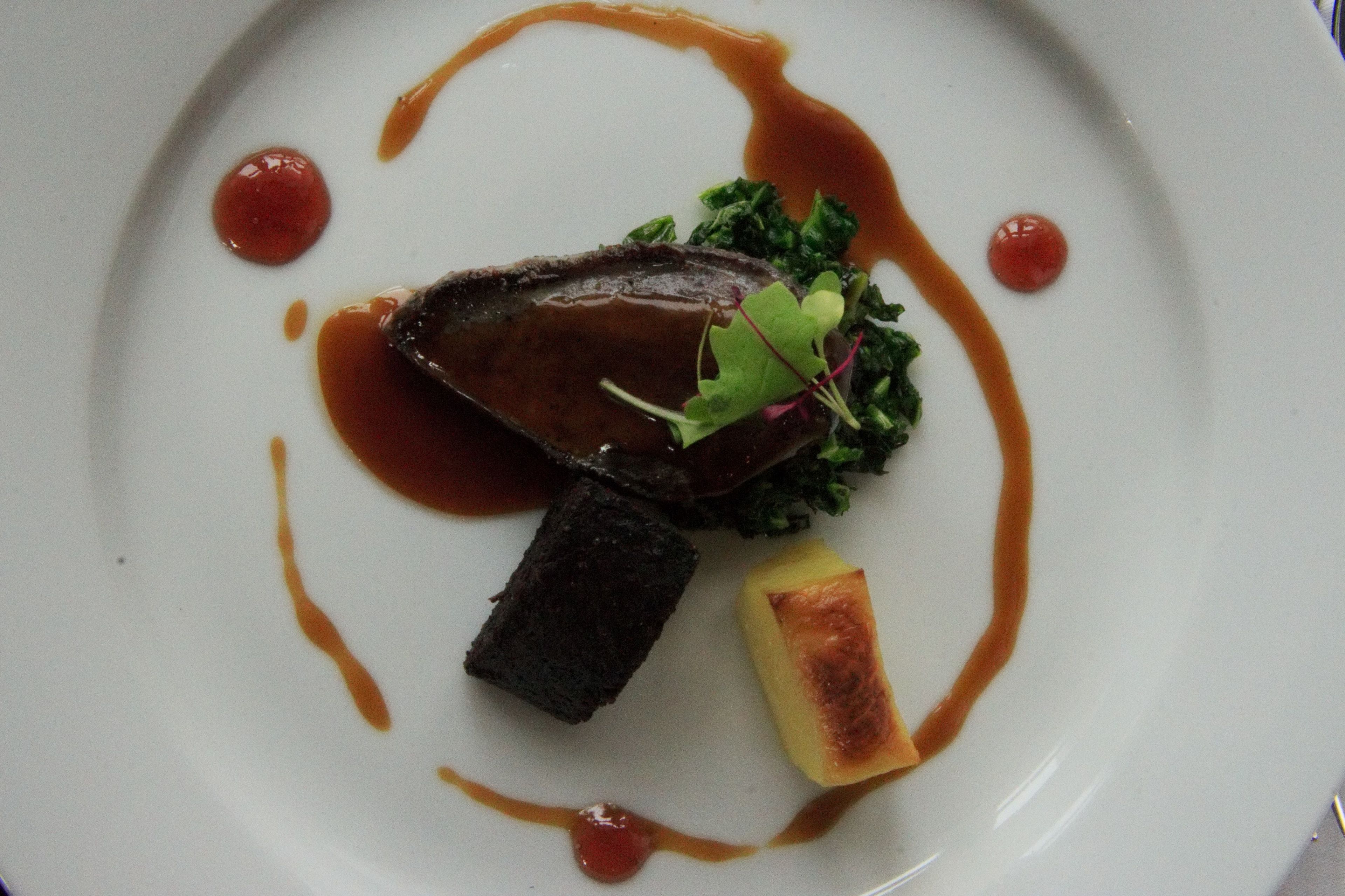 A plate with a piece of meat, a slice of bread, and some greens.