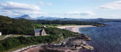 A coastal landscape with a church, beach, and mountains.