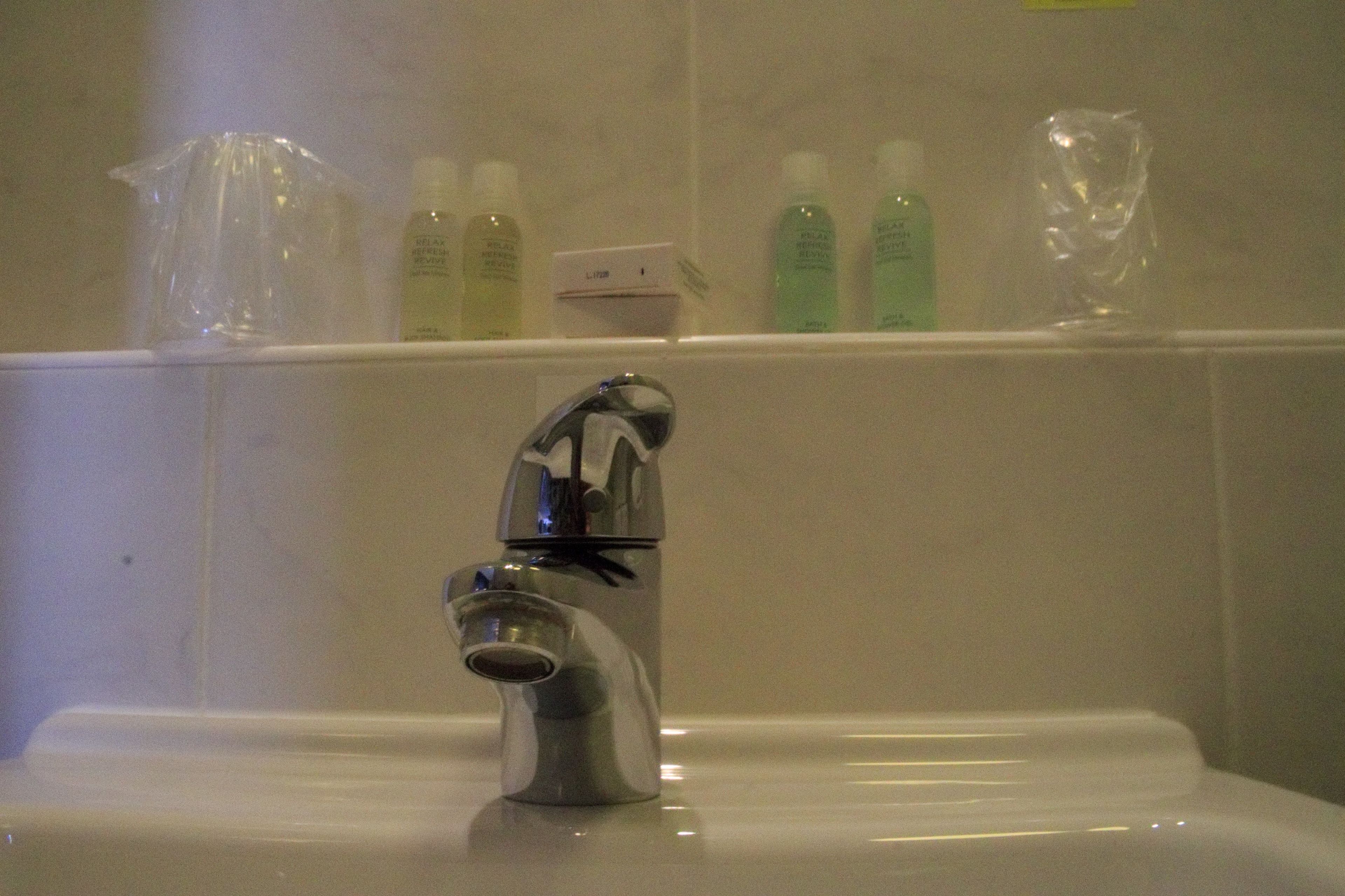 A bathroom sink with a modern faucet, a mirror, and a shelf above holding toiletries.