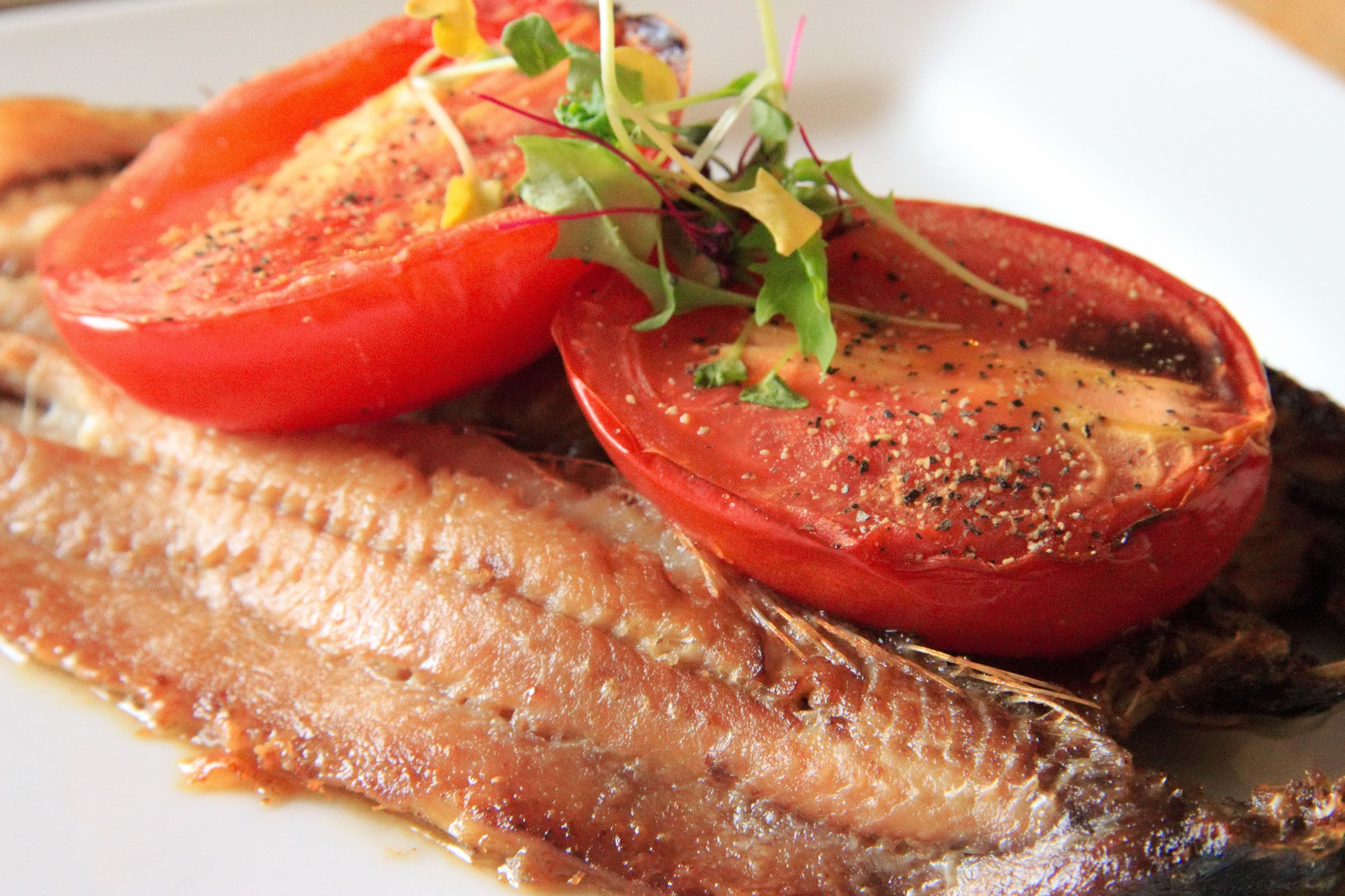 A plate with a grilled fish fillet, tomato slices, and greens.
