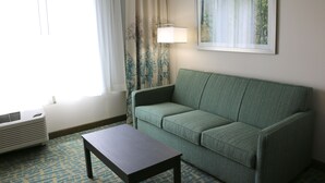 A room with a green sofa, a small table, a lamp, and a painting on the wall.