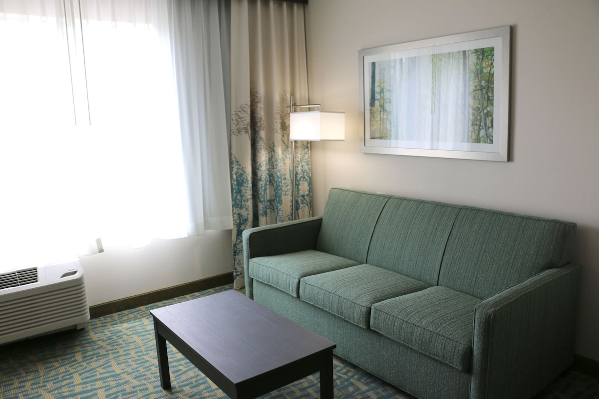 A room with a green sofa, a small table, a lamp, and a painting on the wall.