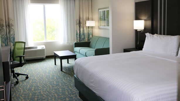 A hotel room with a large bed, a green sofa, a small table, a desk, and a window with curtains.