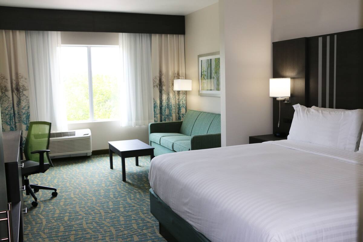 A hotel room with a large bed, a green sofa, a small table, a desk, and a window with curtains.