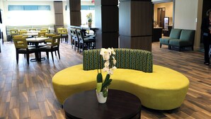 A hotel lobby with a yellow sofa, a round table with a vase of flowers, and a seating area with chairs and tables. - Holiday Inn Express & Suites Hendersonville SE - Flat Rock by IHG (Flat Rock)