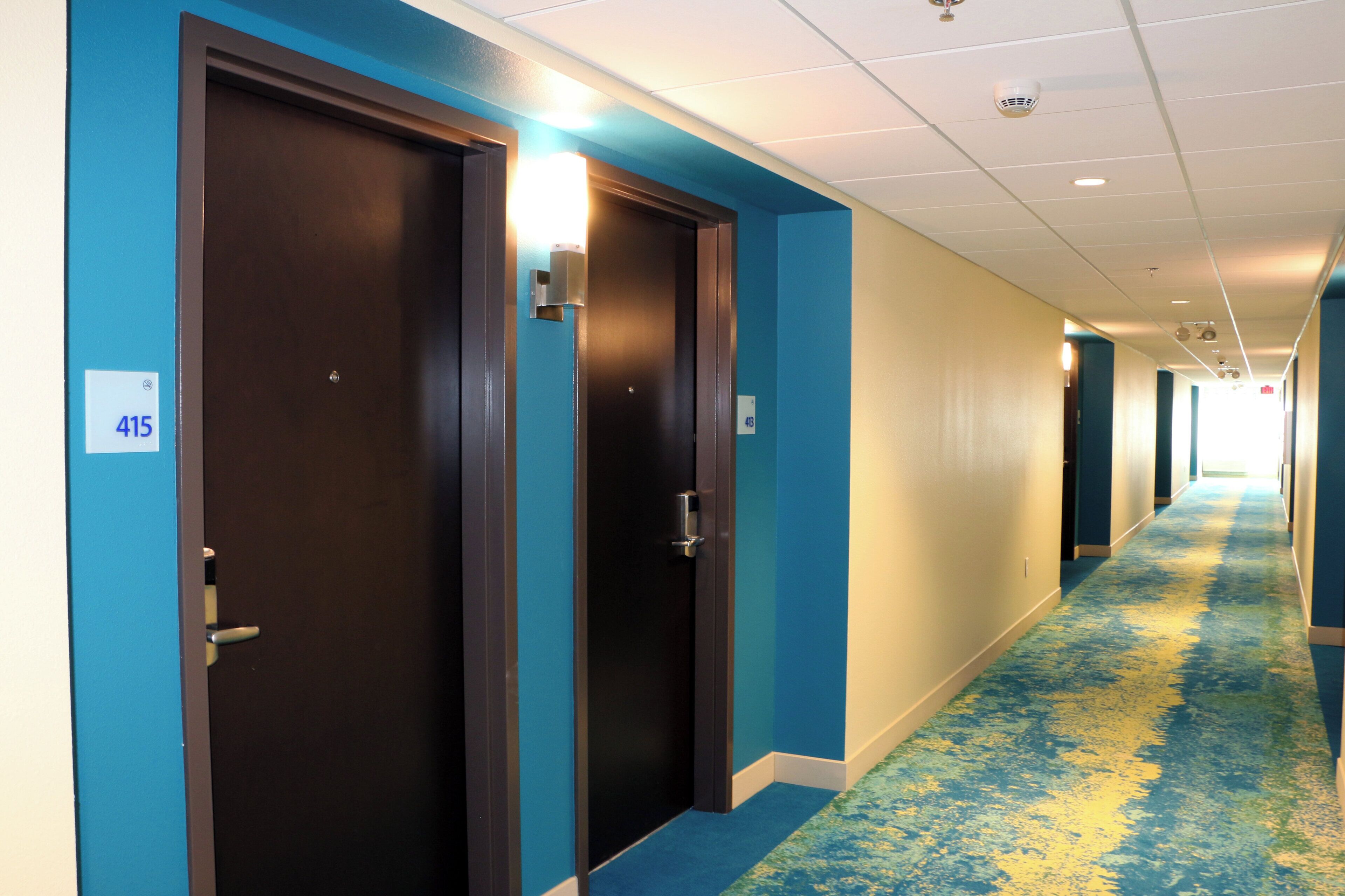 Un corridoio d'albergo con pareti blu, porte numerate e una moquette a motivi.